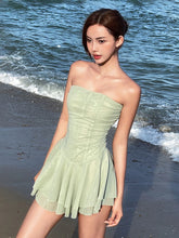 Woman in a light green strapless dress standing on a beach with ocean waves in the background